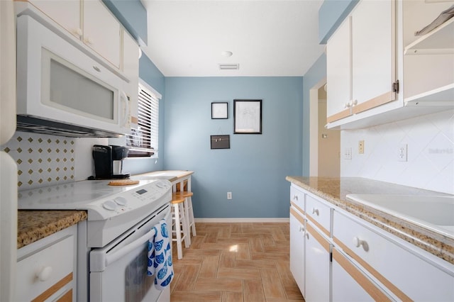 kitchen with light stone countertops, white cabinetry, white appliances, and tasteful backsplash