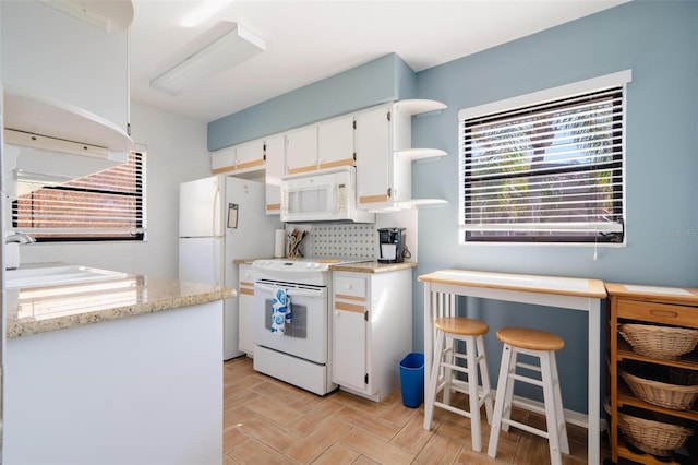 kitchen featuring white appliances, light stone counters, sink, and white cabinets