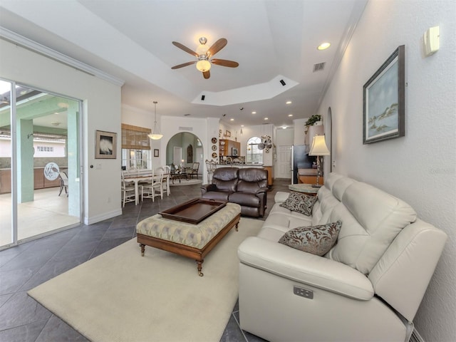 tiled living room with ceiling fan and a raised ceiling