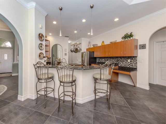 kitchen with dark stone counters, kitchen peninsula, stainless steel refrigerator with ice dispenser, a breakfast bar area, and tasteful backsplash