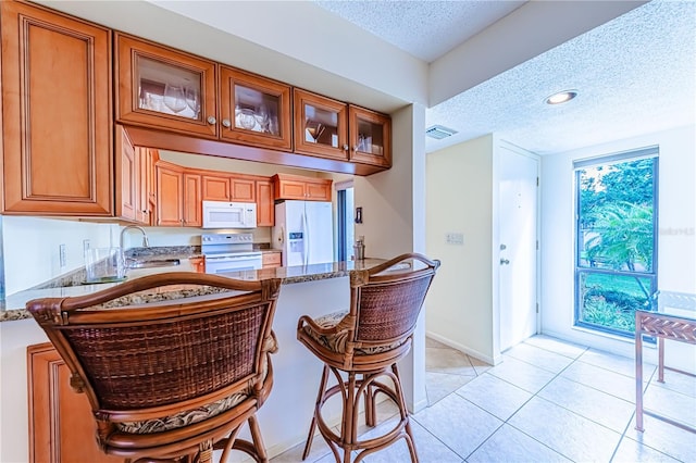 kitchen with a textured ceiling, white appliances, dark stone counters, and light tile patterned flooring