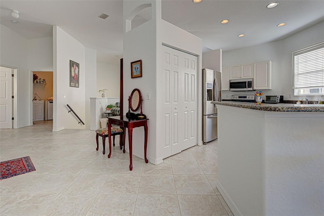 kitchen with appliances with stainless steel finishes, washing machine and clothes dryer, and light tile patterned floors