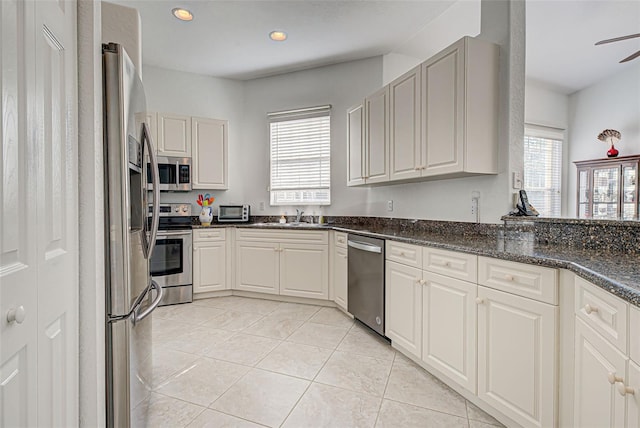 kitchen with ceiling fan, appliances with stainless steel finishes, light tile patterned floors, dark stone counters, and sink