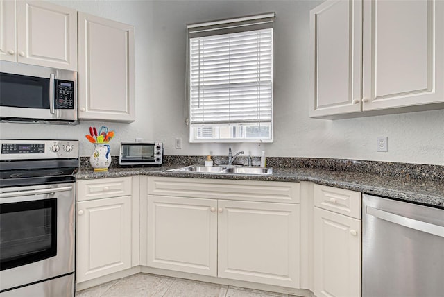 kitchen featuring sink, appliances with stainless steel finishes, white cabinetry, and dark stone countertops