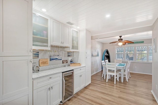 kitchen featuring beverage cooler, light stone countertops, light wood-type flooring, ceiling fan, and white cabinets