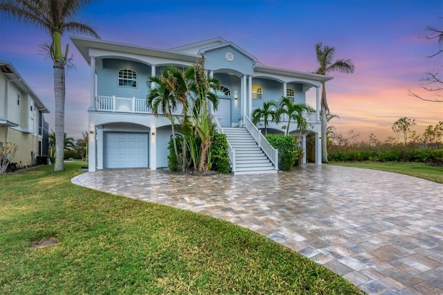 raised beach house featuring a garage, a porch, and a lawn