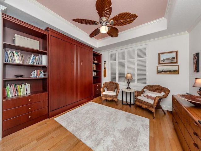 sitting room with crown molding, a raised ceiling, light wood-type flooring, and ceiling fan