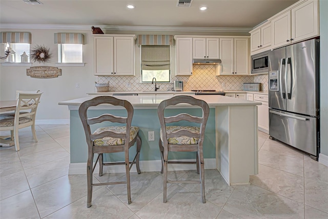 kitchen with crown molding, stainless steel appliances, white cabinetry, a kitchen bar, and a center island