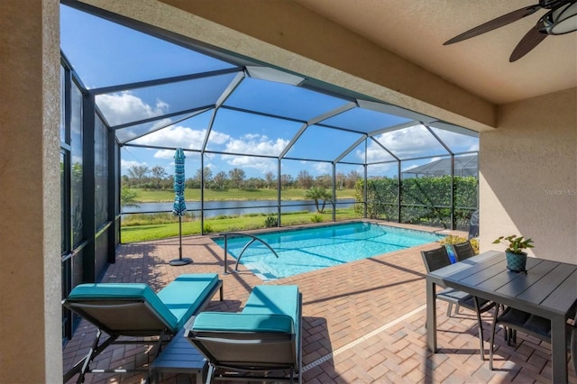 view of pool featuring glass enclosure, ceiling fan, a water view, and a patio