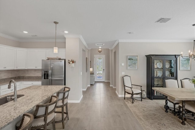 kitchen with white cabinetry, stainless steel refrigerator with ice dispenser, light stone countertops, pendant lighting, and sink