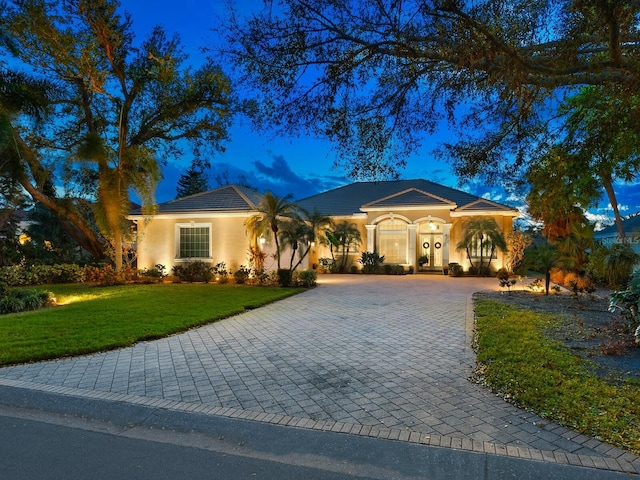 mediterranean / spanish home with stucco siding, a tiled roof, decorative driveway, and a yard