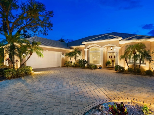 mediterranean / spanish-style house featuring decorative driveway, an attached garage, a tile roof, and stucco siding