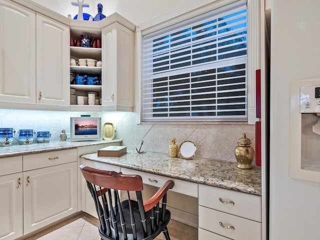 kitchen with built in desk, light stone counters, tasteful backsplash, light tile patterned floors, and white cabinets