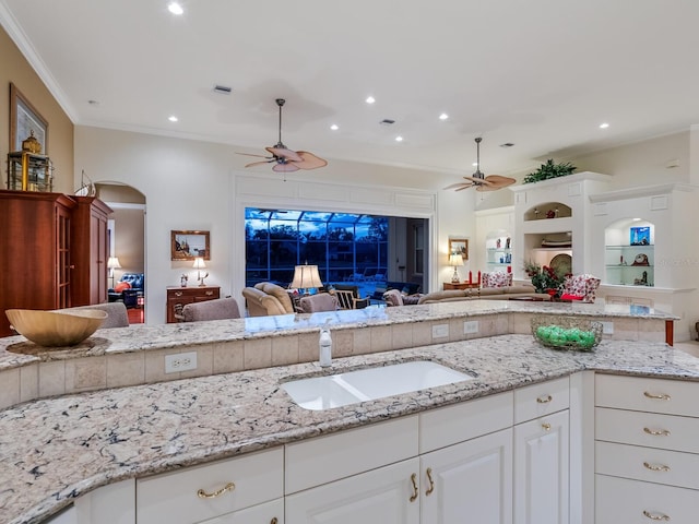 kitchen featuring sink, light stone counters, ceiling fan, crown molding, and white cabinets