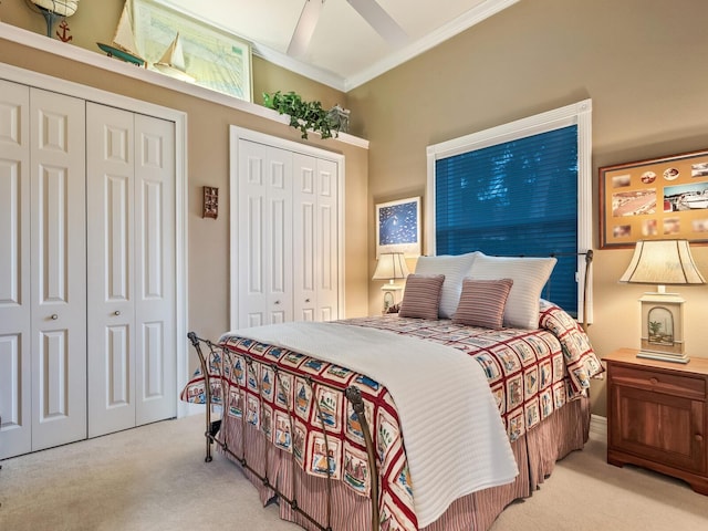 bedroom with ornamental molding, light colored carpet, ceiling fan, and two closets