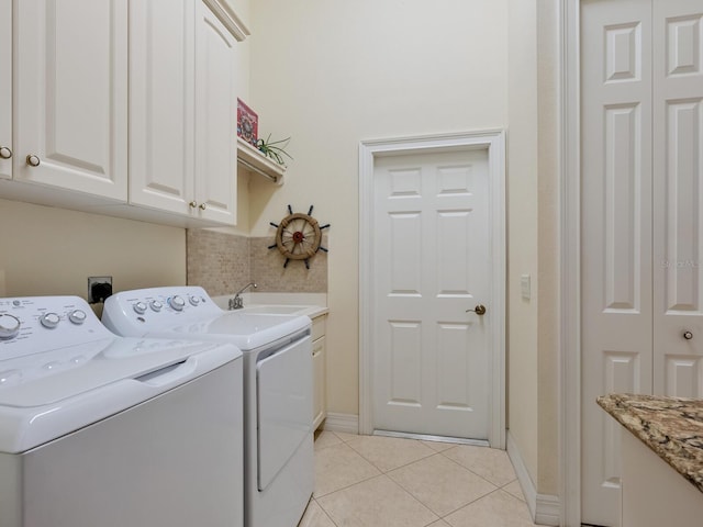 washroom with light tile patterned floors, washing machine and dryer, a sink, baseboards, and cabinet space