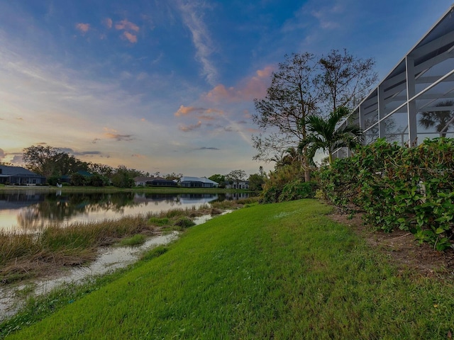 yard at dusk featuring a water view and a lanai