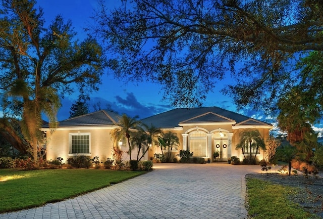 mediterranean / spanish-style house with a tiled roof, a yard, driveway, and stucco siding