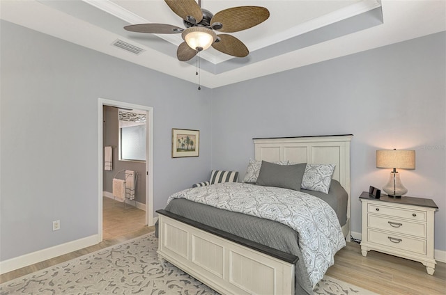 bedroom featuring ensuite bath, ceiling fan, crown molding, light hardwood / wood-style floors, and a tray ceiling