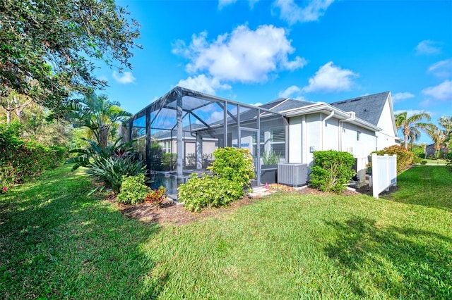 rear view of house with central AC unit, a lanai, and a lawn