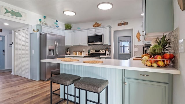 kitchen with decorative backsplash, stainless steel appliances, light hardwood / wood-style flooring, and a breakfast bar area