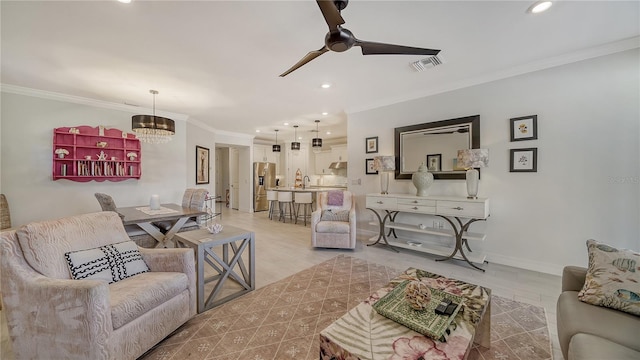 living room with ceiling fan with notable chandelier, light hardwood / wood-style floors, ornamental molding, and sink