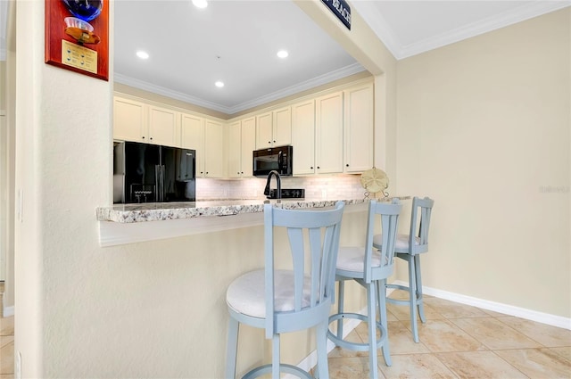 kitchen featuring a breakfast bar area, decorative backsplash, black appliances, and cream cabinetry