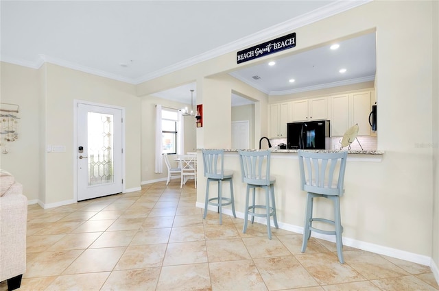 kitchen with a breakfast bar, black fridge, crown molding, light stone counters, and kitchen peninsula