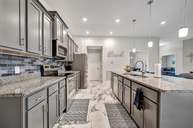 kitchen with a center island with sink, decorative backsplash, hanging light fixtures, sink, and appliances with stainless steel finishes