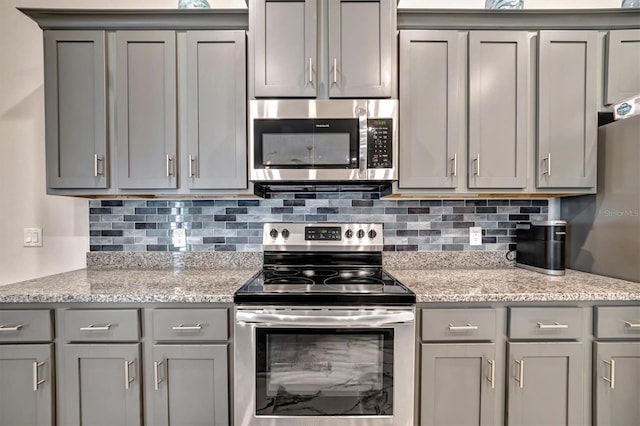 kitchen with gray cabinets, appliances with stainless steel finishes, and light stone counters