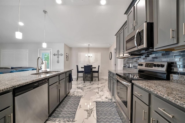 kitchen with light stone counters, backsplash, appliances with stainless steel finishes, decorative light fixtures, and sink