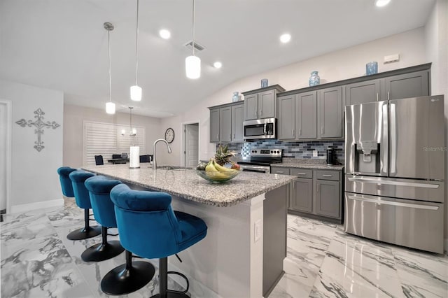 kitchen with stainless steel appliances, a kitchen bar, hanging light fixtures, sink, and a kitchen island with sink