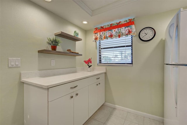 kitchen with ornamental molding, light tile patterned floors, white fridge, and white cabinets