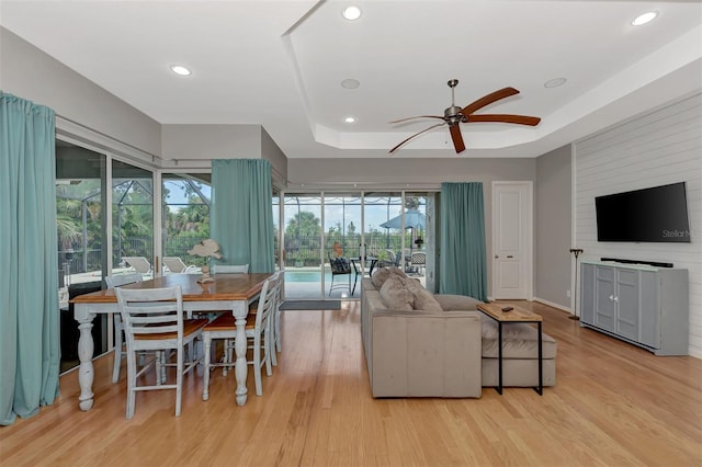 living room featuring light hardwood / wood-style flooring, a tray ceiling, and ceiling fan