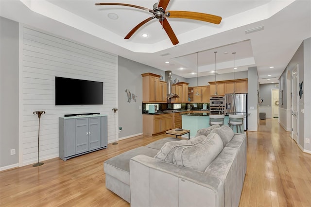 living room with ceiling fan, light wood-type flooring, and a raised ceiling