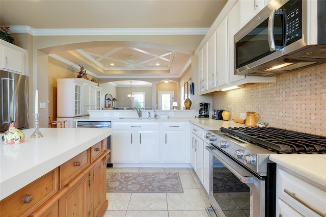 kitchen with coffered ceiling, backsplash, crown molding, white cabinetry, and appliances with stainless steel finishes