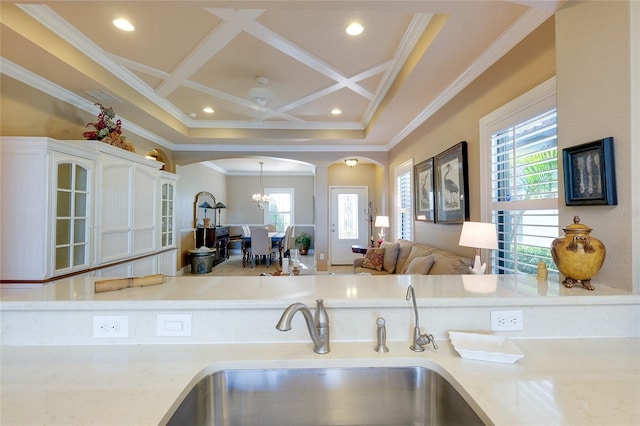 kitchen with white cabinets, ceiling fan with notable chandelier, crown molding, sink, and coffered ceiling