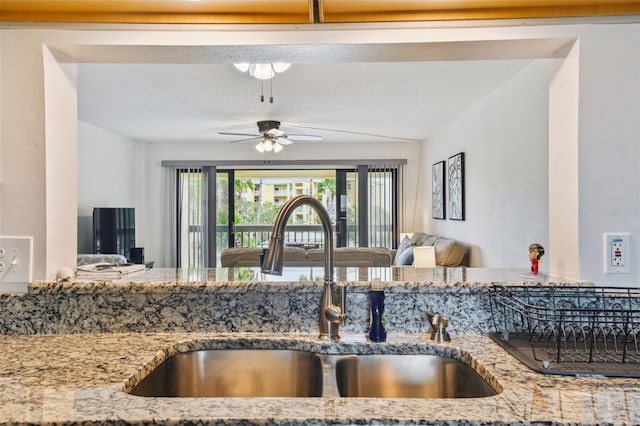 kitchen featuring light stone countertops, a textured ceiling, ceiling fan, and sink