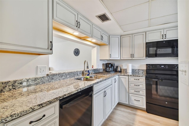 kitchen featuring light stone countertops, light hardwood / wood-style flooring, black appliances, and sink