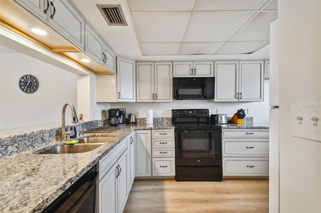 kitchen with light stone countertops, a drop ceiling, sink, black appliances, and light hardwood / wood-style floors