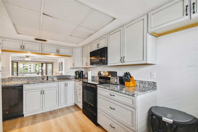 kitchen featuring light stone counters, ceiling fan, sink, black appliances, and light hardwood / wood-style floors