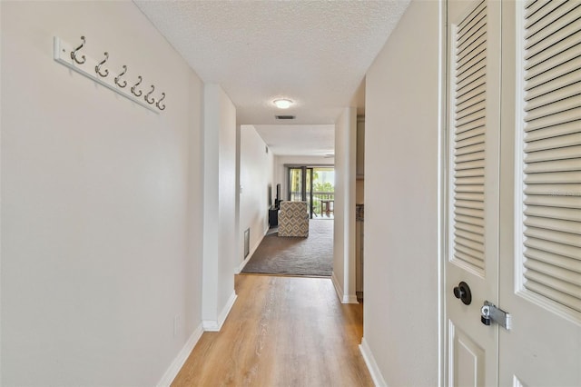 hall with a textured ceiling and light hardwood / wood-style floors