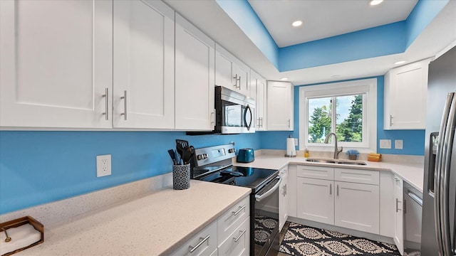 kitchen with white cabinets, appliances with stainless steel finishes, light stone countertops, and sink