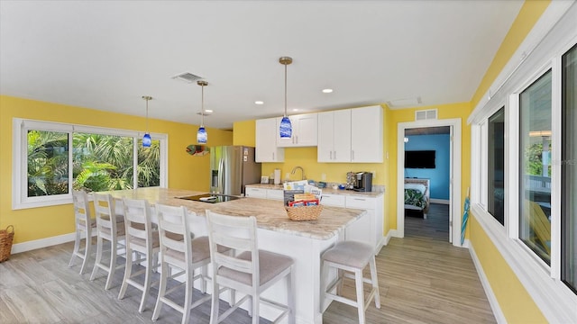 kitchen featuring a center island with sink, stainless steel refrigerator with ice dispenser, light wood-type flooring, decorative light fixtures, and white cabinetry