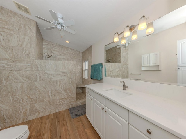 bathroom with hardwood / wood-style flooring, a tile shower, vanity, toilet, and vaulted ceiling