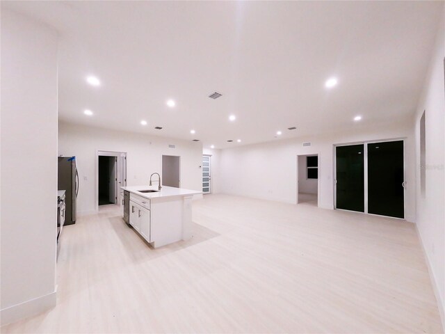 kitchen featuring stainless steel refrigerator, sink, an island with sink, white cabinets, and light hardwood / wood-style flooring