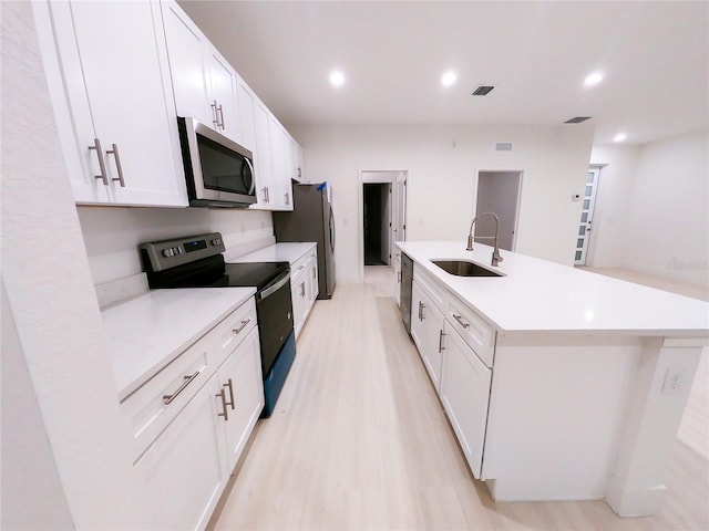 kitchen featuring sink, an island with sink, white cabinetry, light wood-type flooring, and appliances with stainless steel finishes