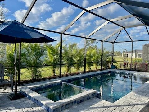 view of pool featuring a patio, glass enclosure, and an in ground hot tub