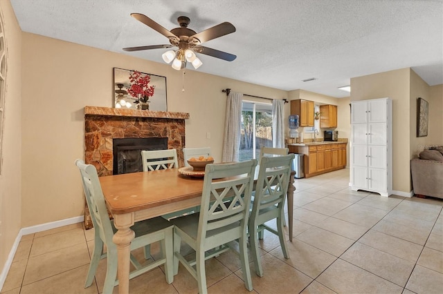 dining space featuring ceiling fan, sink, a textured ceiling, a fireplace, and light tile patterned flooring