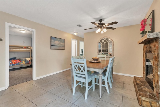 dining room featuring tile patterned floors, a stone fireplace, ceiling fan, and a textured ceiling